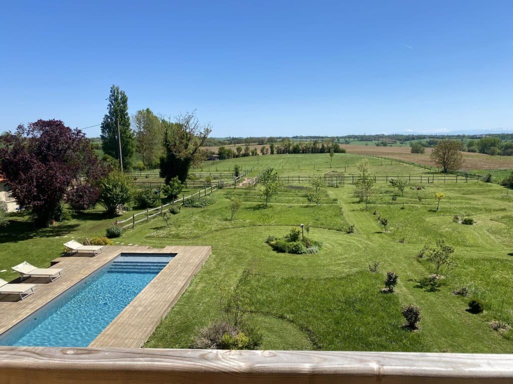 Vue depuis la terrasse de la cabane sur la piscine, le jardin et les coteaux du Lauragais